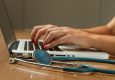 Close-up of hands typing on a laptop with a stethoscope in the foreground.